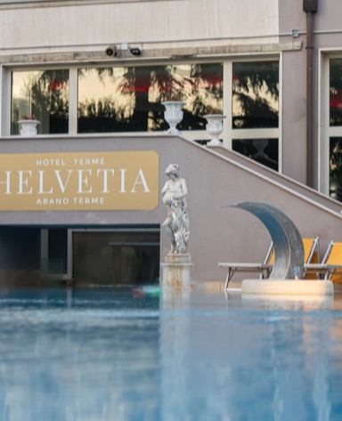 Una piscina di un hotel termale con una statua in stile classico e un'insegna che dice "Hotel Terme Helvetia".