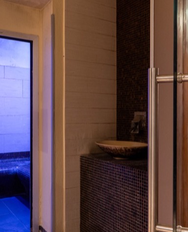 Interno di un bagno moderno con pareti in piastrelle scure, lavabo elegante e luce blu soffusa sullo sfondo.