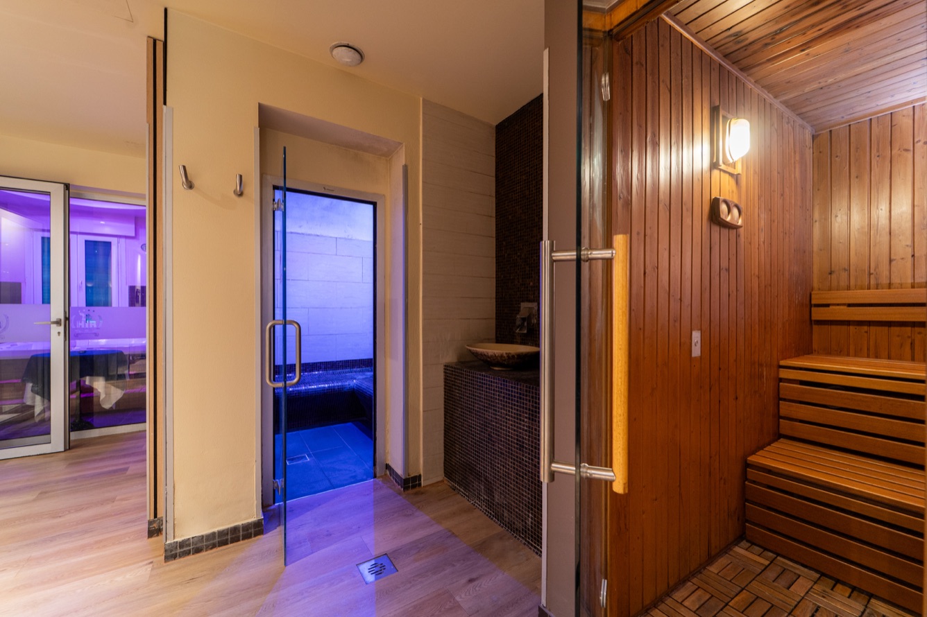 Interno di una sauna con lampade blu, porte in vetro e dettagli in legno, creando un'atmosfera rilassante.