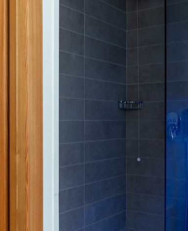 Doccia moderna con pareti in piastrelle grigie e porta in vetro, attrezzata con doccetta e mensola.