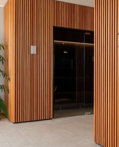 Interno moderno con pareti in legno a listelli e una porta a vetri, circondato da piante verdi.